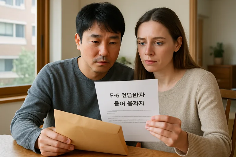 한국인 남편과 외국인 아내가 식탁에 앉아 F-6 결혼비자 불허 통지서와 서류 봉투를 함께 살펴보는 모습, 결혼이민 비자 재신청